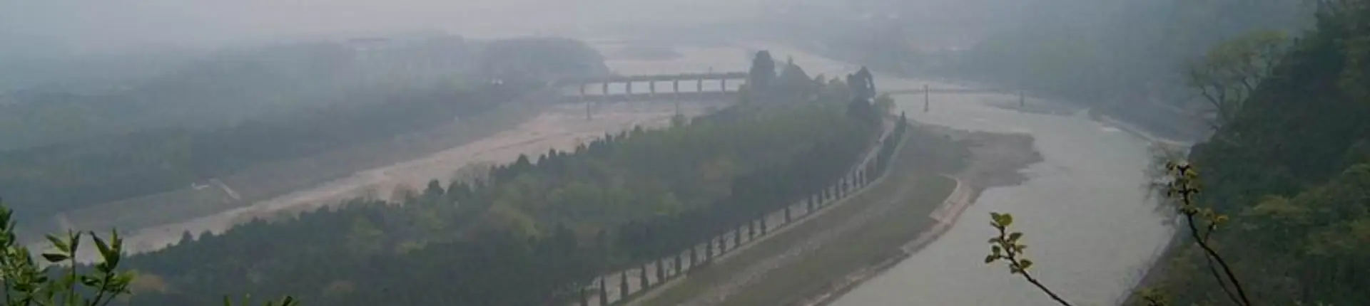 Broad river divided by long tree-lined embankments beneath a misty sky