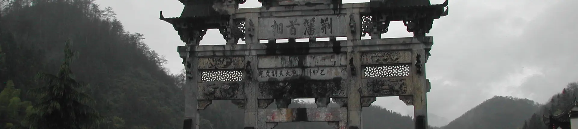 Ornate carved stone archway beside misty hills at Xidi Village, Anhui