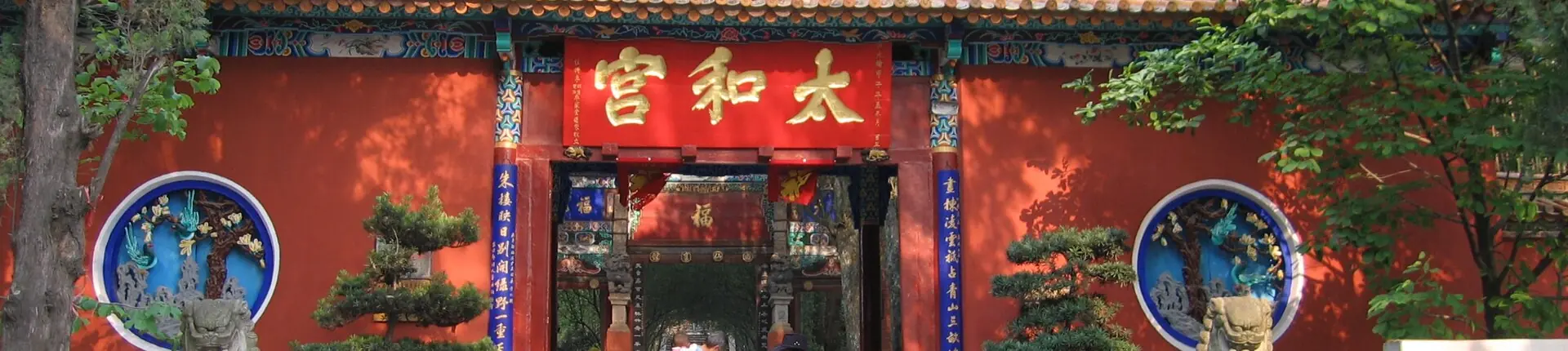 Painted red temple entrance with gold lettering and round decorations at Golden Temple, Kunming