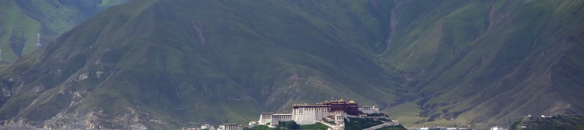 Small white hermitage buildings beneath grassy mountain slopes at Pabonka near Lhasa