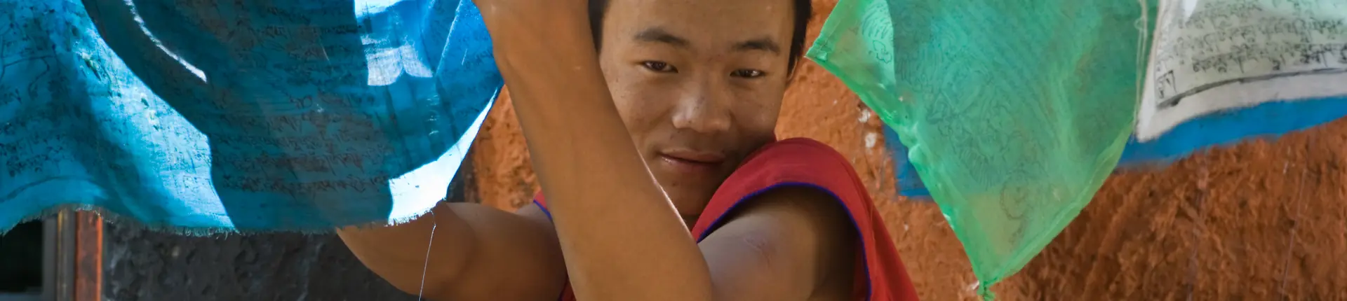Young monk holding colorful prayer flags close to his face in Tibet