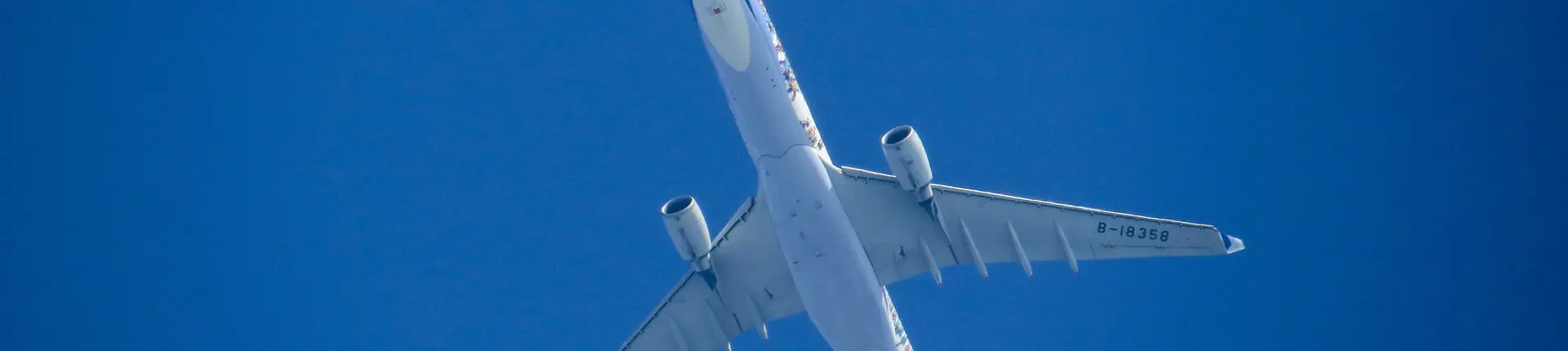 Underside of a passenger jet with its wings and engines against a blue sky