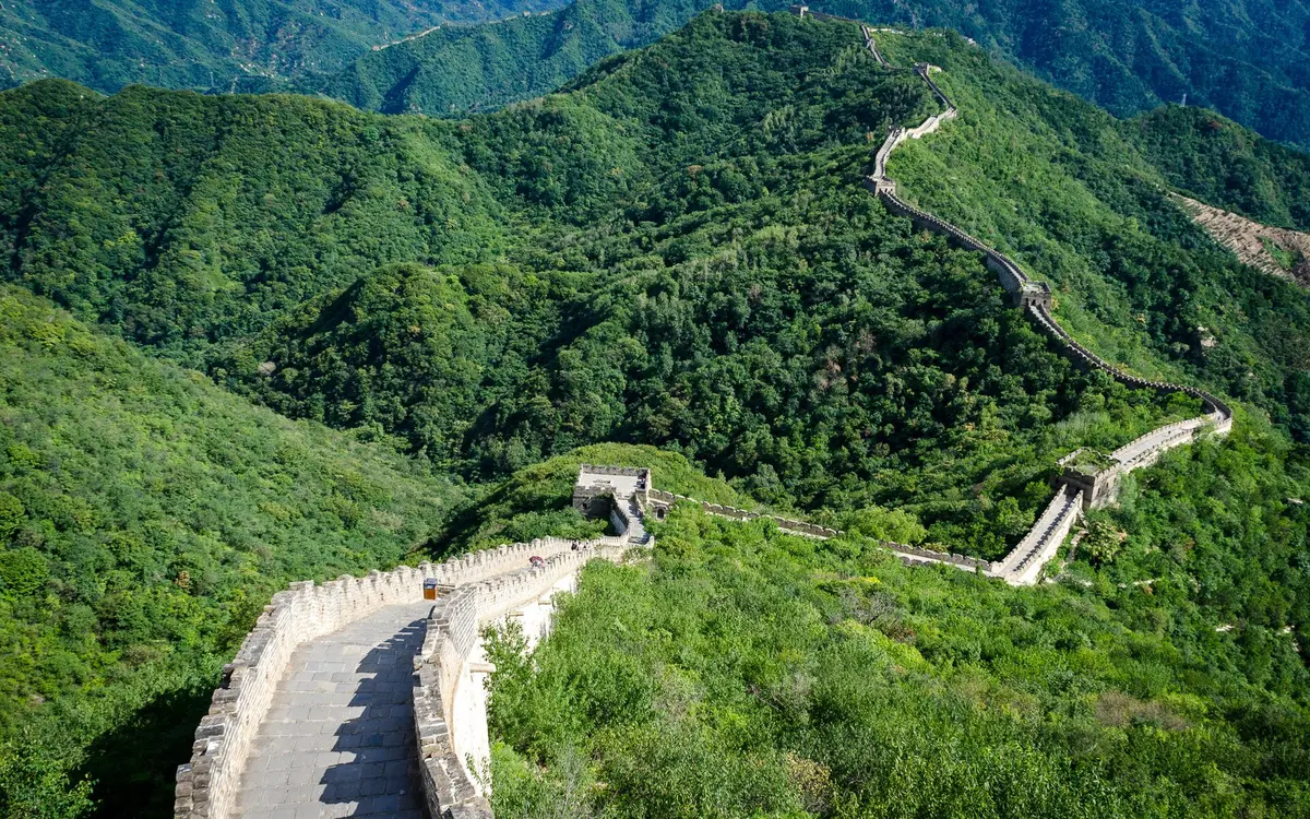 Great Wall towers and battlements crossing densely wooded green mountain ridges
