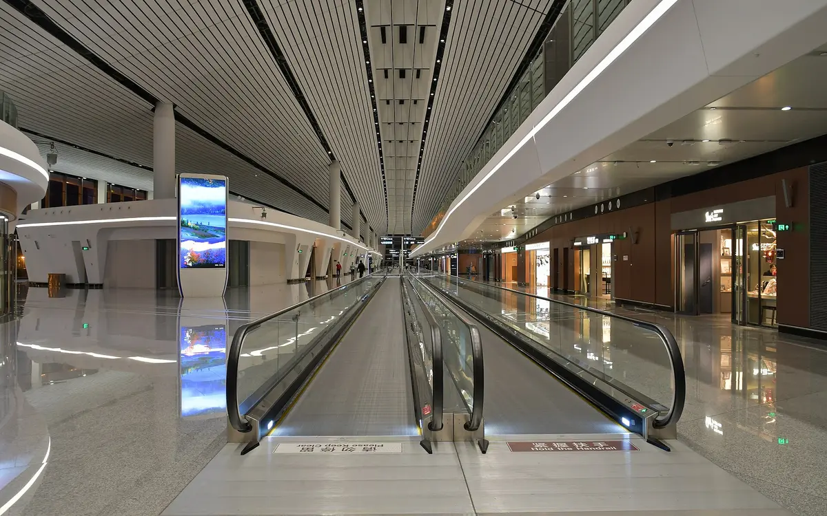 Pasillo de aeropuerto vacío con pasillos móviles y suelo de baldosas reflectante