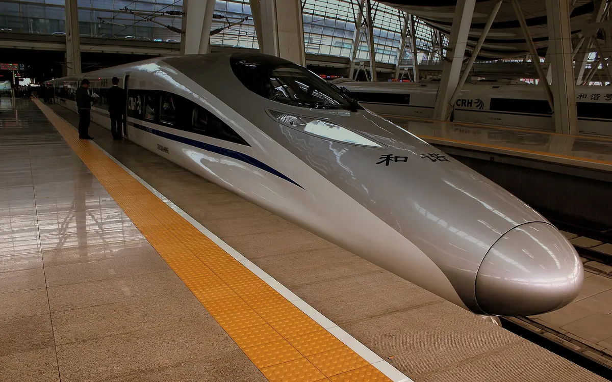 Silver high-speed train beside a yellow tactile strip under a station canopy