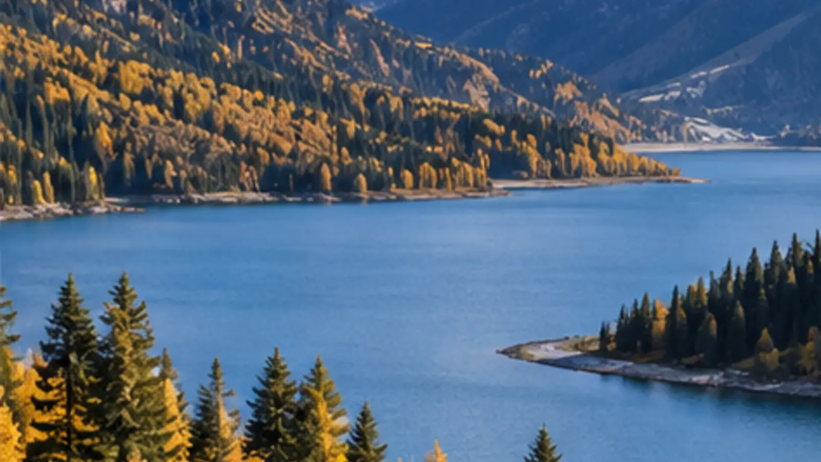 Blue alpine lake surrounded by golden autumn woodland and dark mountains