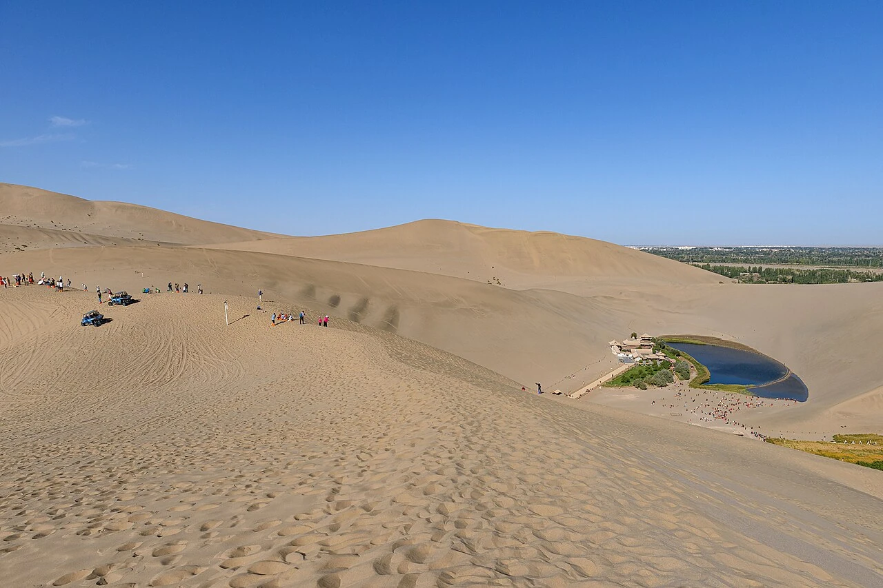 Mondsichelförmiger Oasensee zwischen weiten goldenen Dünen bei Dunhuang