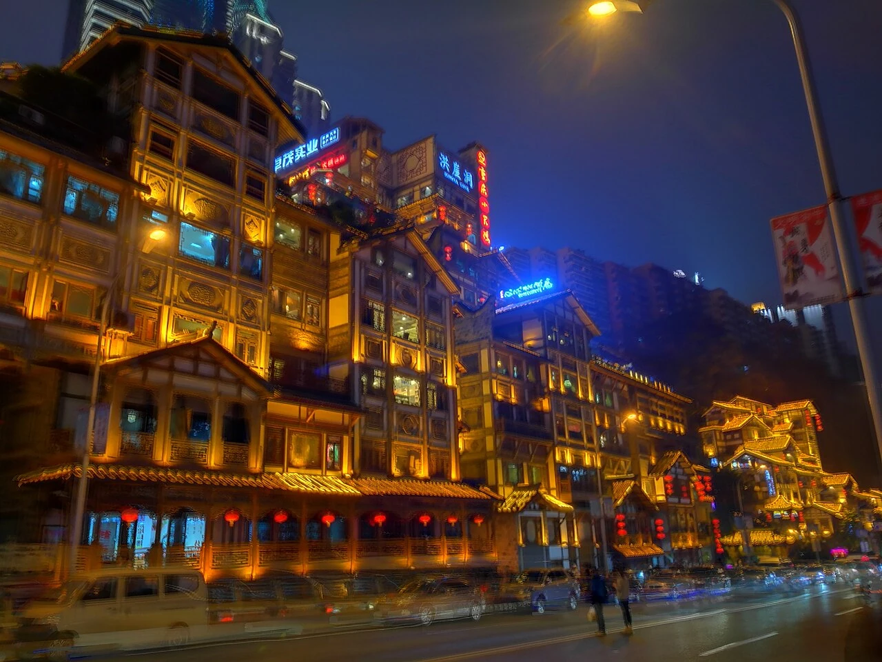 Les bâtiments à étages de Hongyadong illuminés en doré au bord d’une rue de Chongqing, la nuit