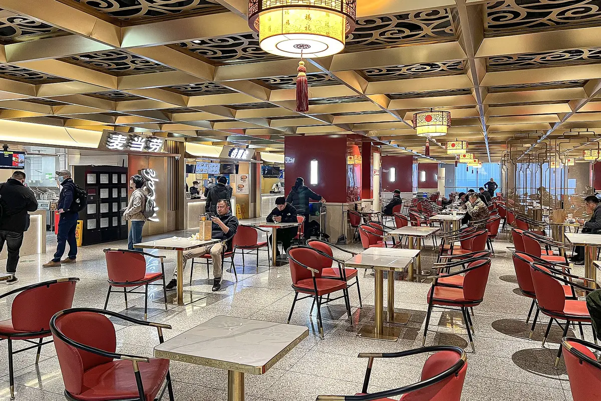 Restaurant dining hall with red chairs beneath an ornate coffered ceiling