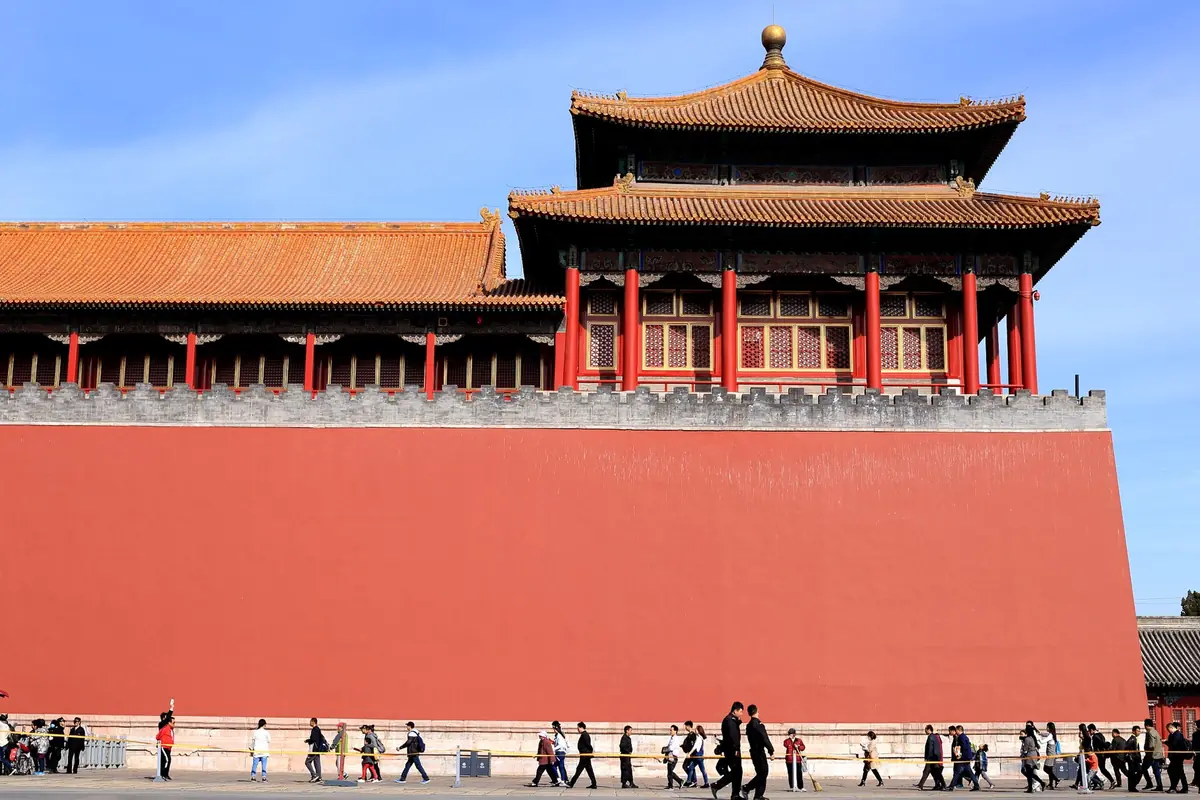 Visitors beside the Forbidden City's red wall and golden palace roofs in Beijing
