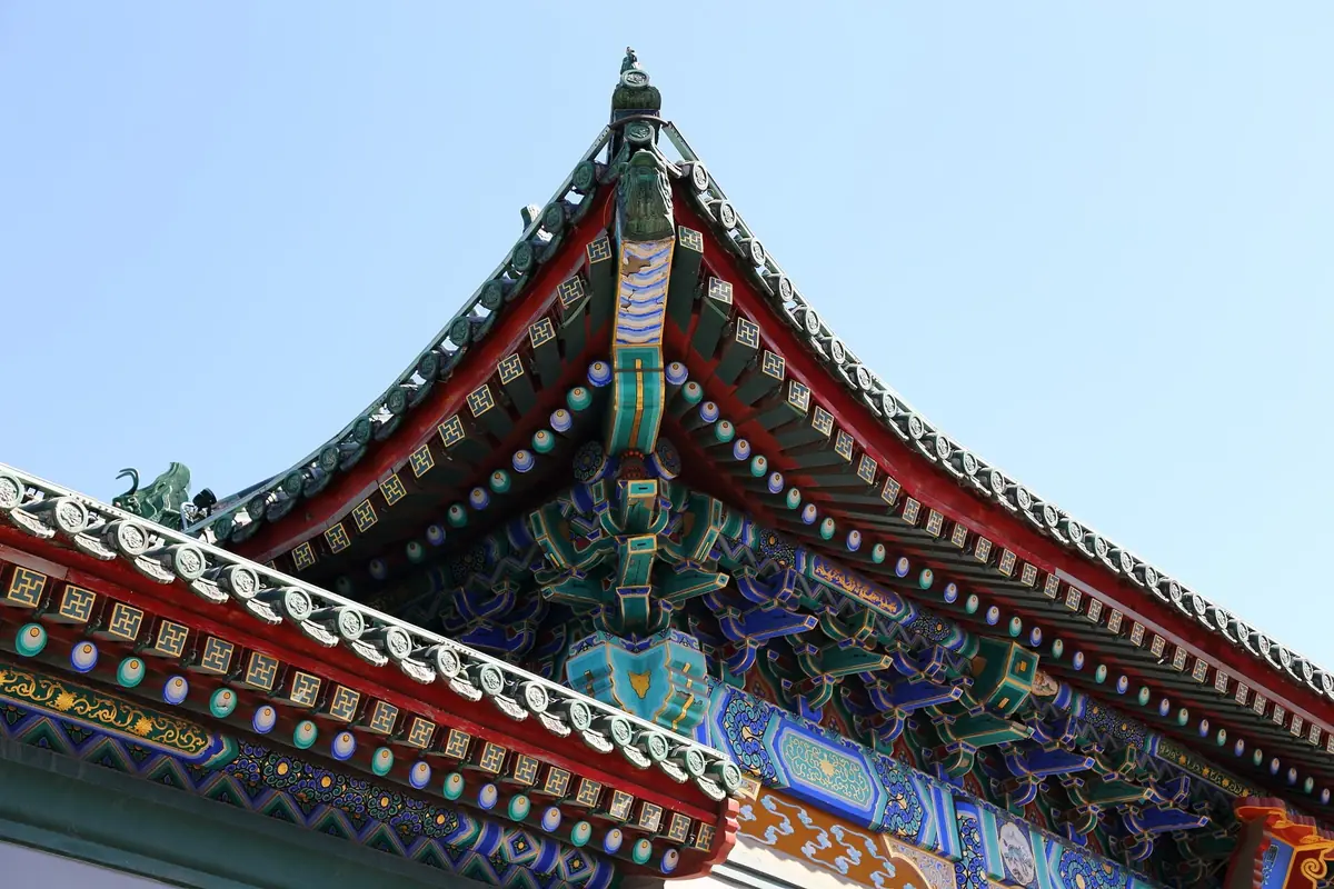 Close view of richly painted traditional roof beams beneath gray curved tiles