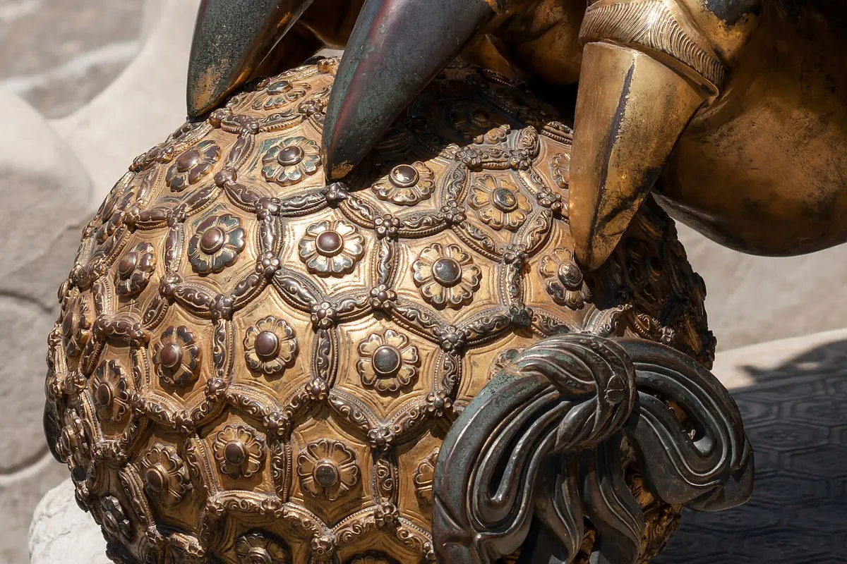 Bronze guardian lion's paw resting on an elaborately carved ball
