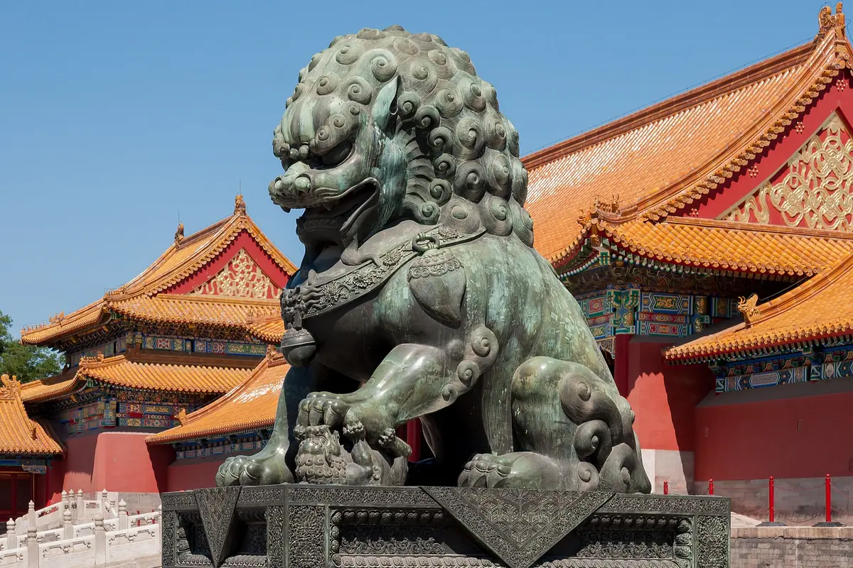Bronze guardian lion outside the Forbidden City's red-and-gold palace buildings in Beijing