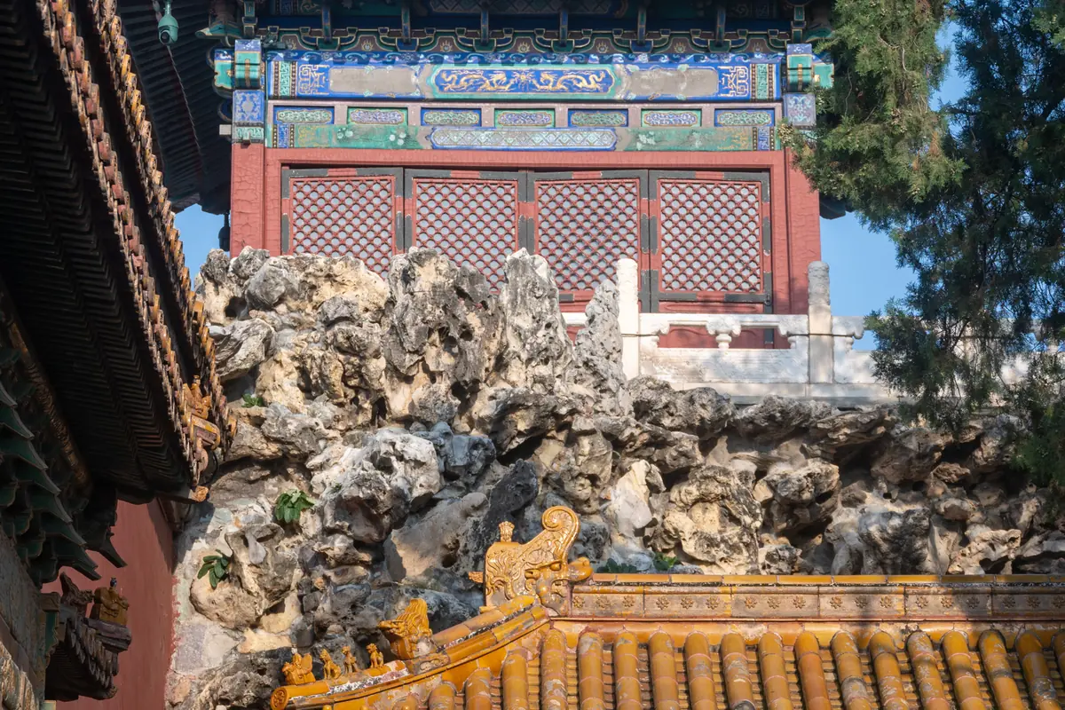 Ornamental limestone rockery behind a golden fence beside painted palace buildings