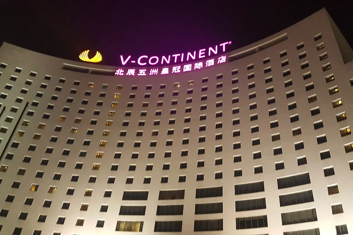 Curved V-Continent hotel facade with illuminated purple signage at night