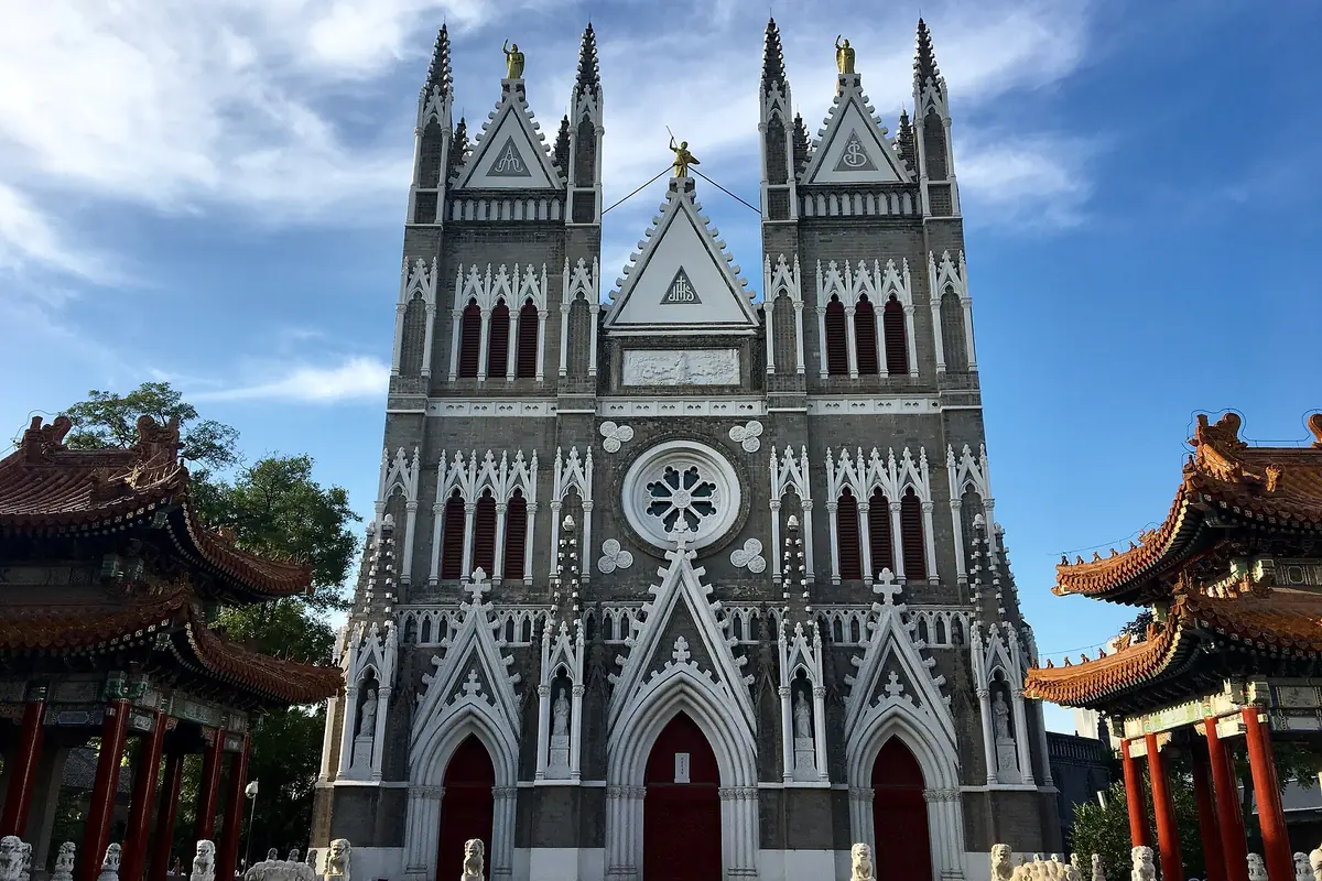 Tall black-and-white church facade framed by traditional tiled roofs and green trees