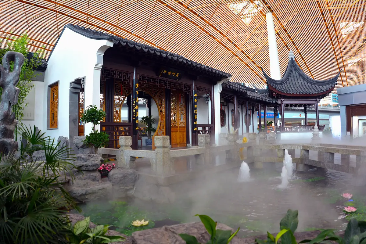Indoor garden with traditional pavilion roofs, plants and mist beneath a wooden ceiling