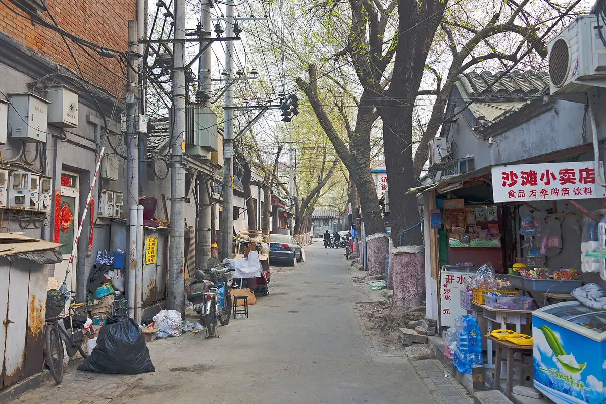 Schmale Pekinger Gasse mit kleinen Läden, Oberleitungen und kahlen Bäumen
