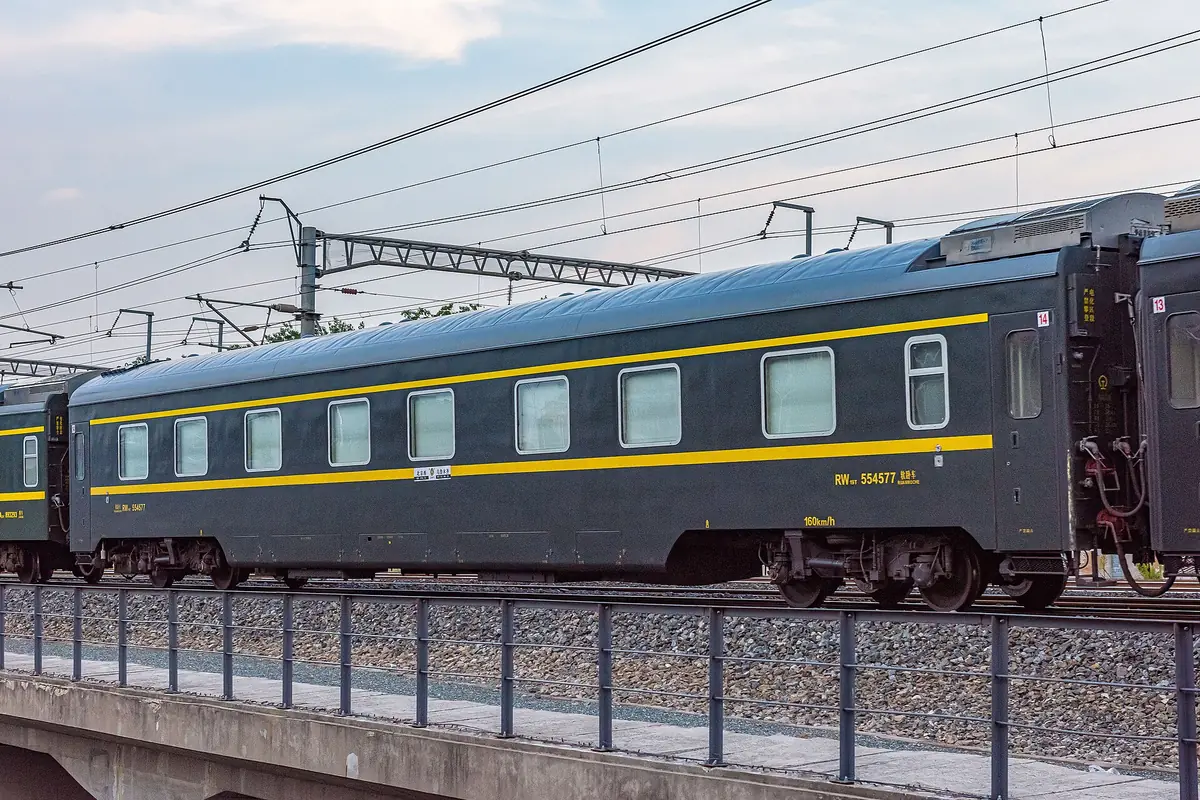 Blue-and-yellow passenger train carriage beneath overhead railway wires