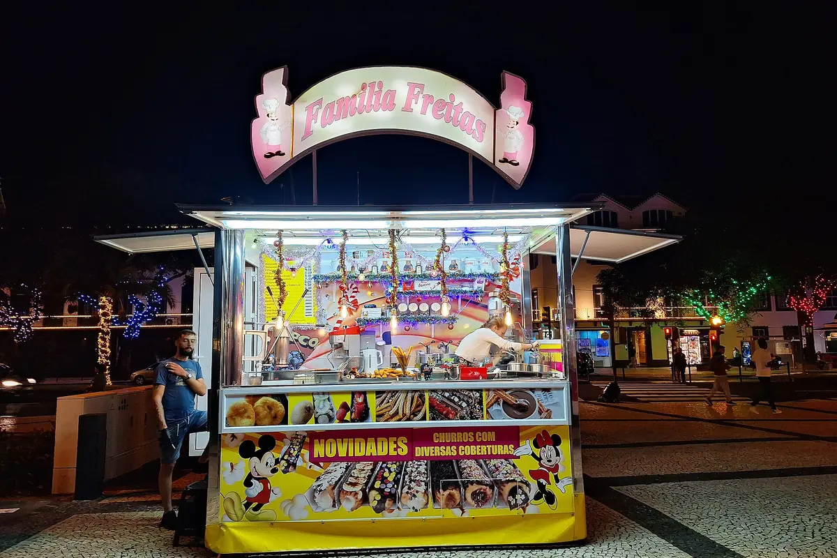 Brightly illuminated street-food kiosk beneath a decorative sign at night