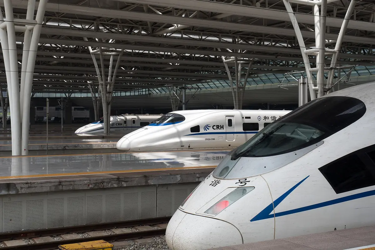 White high-speed trains on parallel tracks beneath a broad station canopy