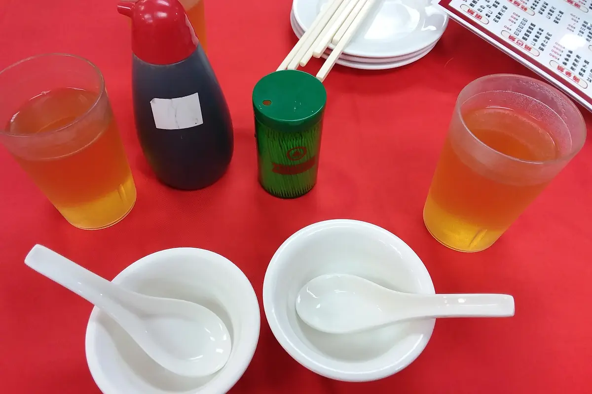 White bowls and spoons beside drinks and condiments on a red dining table