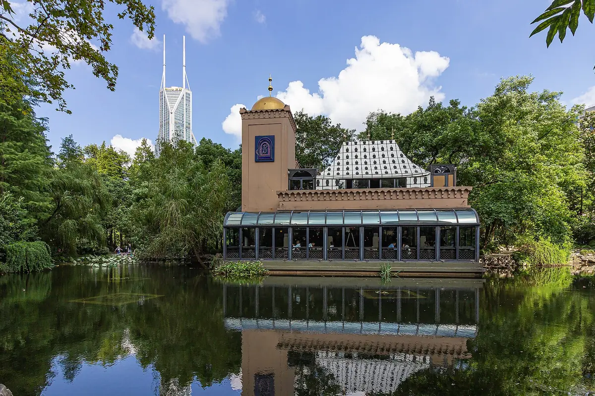 Lakeside building with a clock tower reflected in still water among green trees