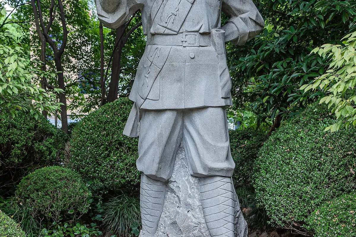 Stone statue in traditional clothing among dense green park shrubs