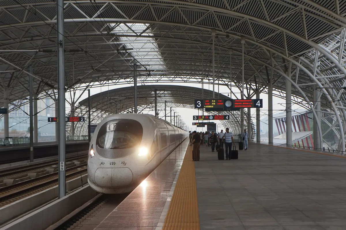White high-speed train beside a covered station platform with illuminated headlights