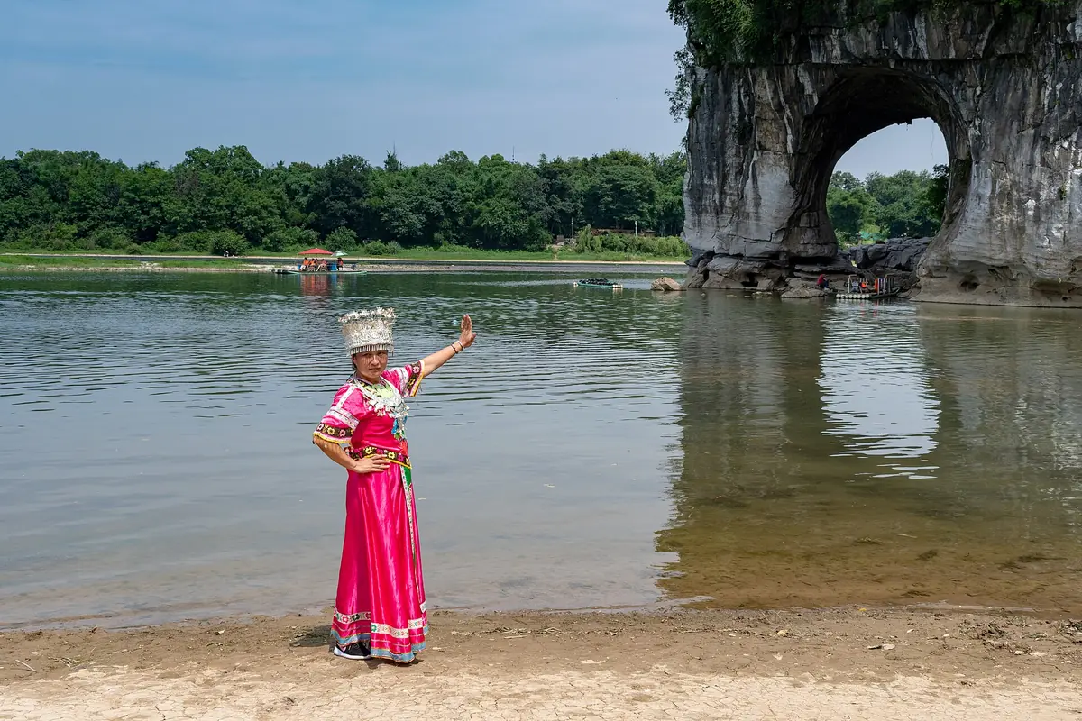 Woman in a bright pink dress posing beside water at Elephant Trunk Hill