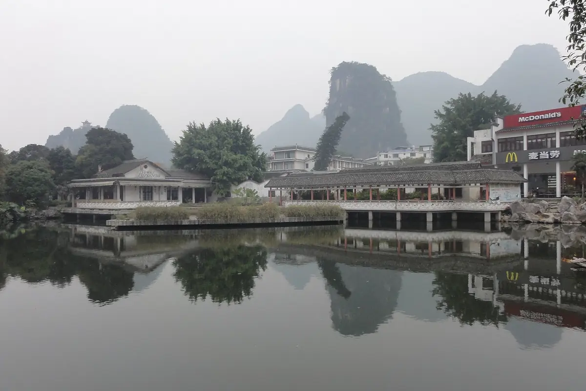 Waterfront pavilions and buildings reflected in a still lake beneath distant karst peaks