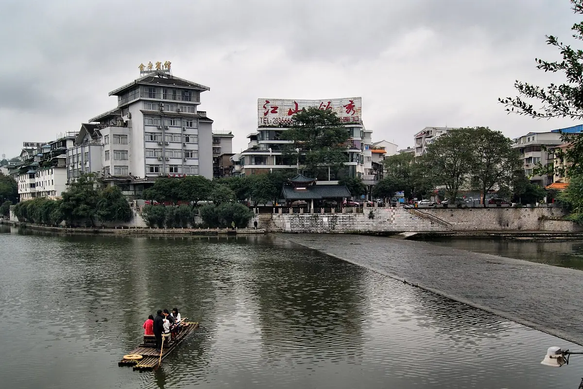 Petit bateau sur un lac, près de bâtiments riverains et d’une pagode à étages