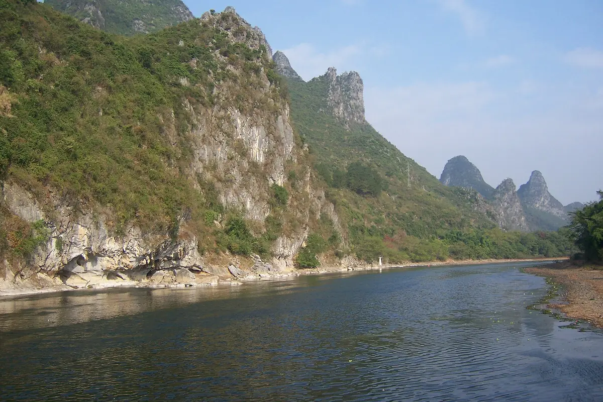 Acantilado escarpado de piedra caliza junto a un río azul y picos kársticos verdes a lo lejos