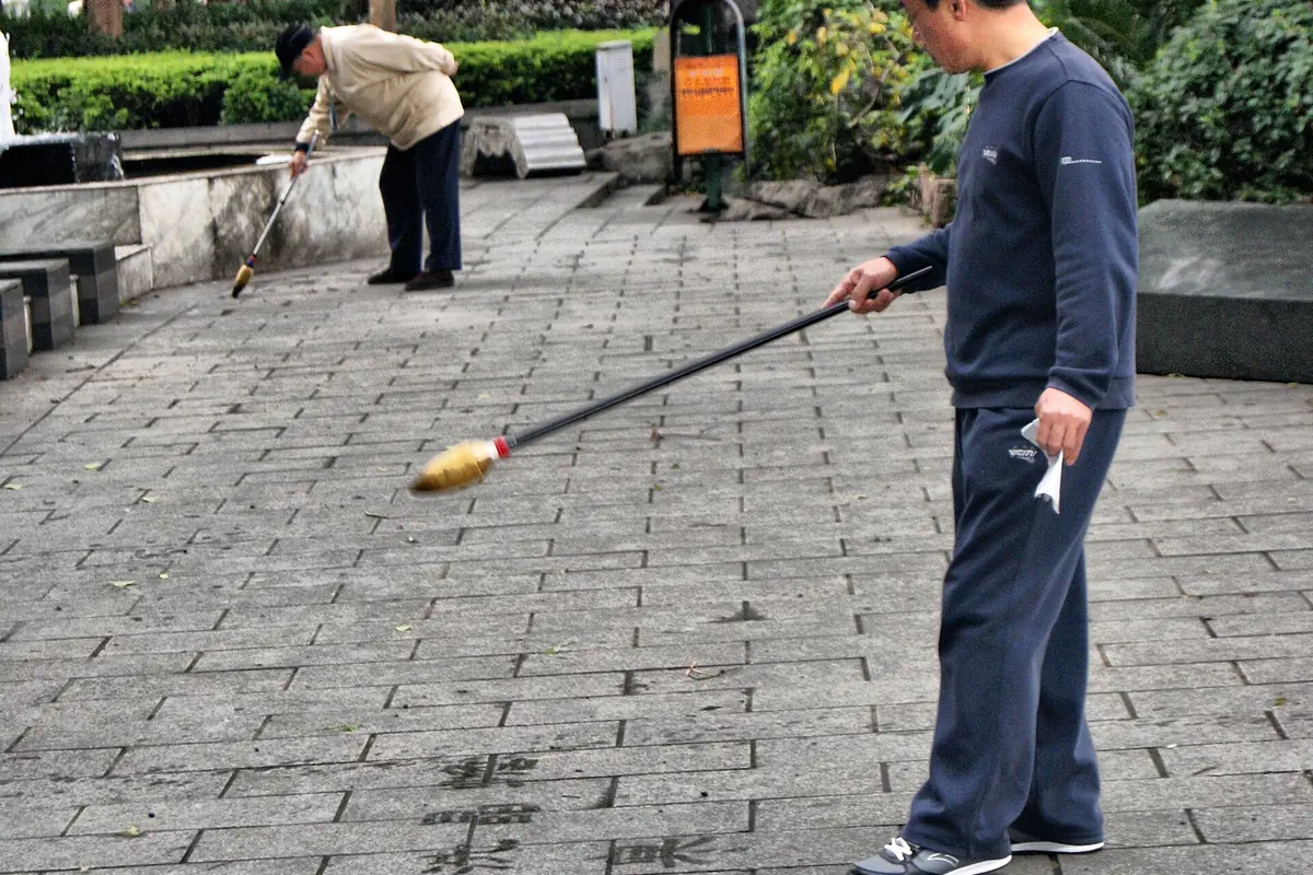 Person holding a long pole with a small colorful object above a paved park terrace