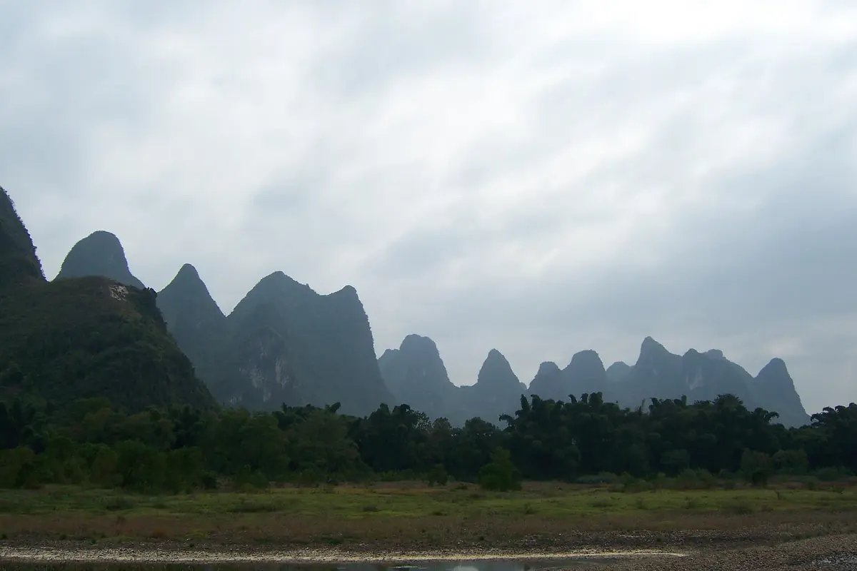 Rows of dark karst peaks above a wooded plain beneath thick clouds