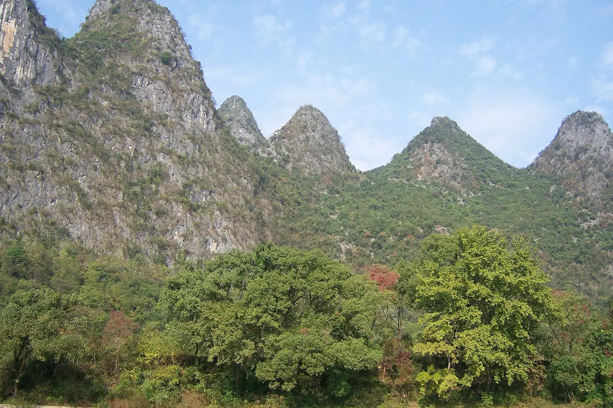 Rugged karst peaks rising above dense trees beneath scattered clouds