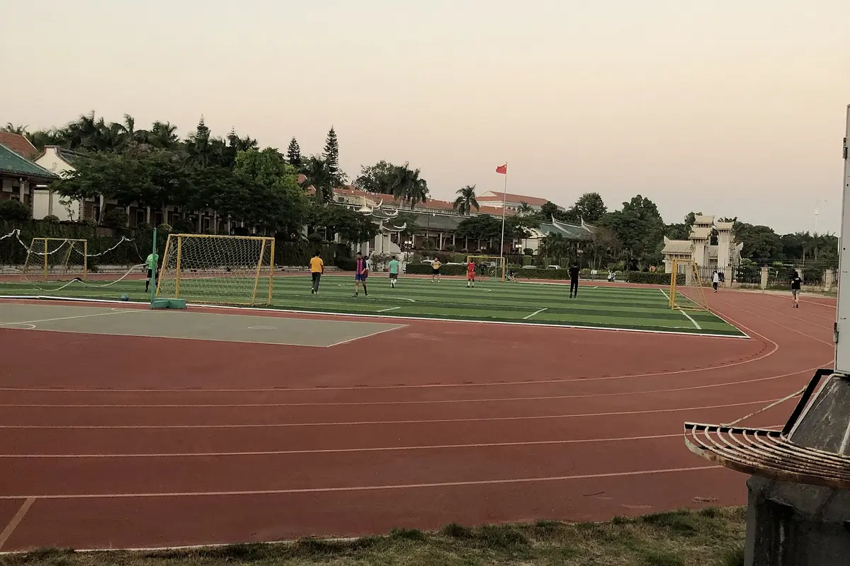 Piste d’athlétisme rouge autour d’un terrain de sport vert, près de bâtiments traditionnels