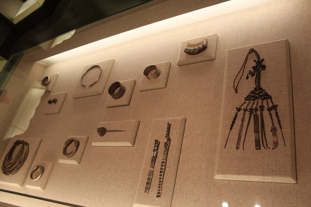 Metal ornaments, necklaces and belts mounted on an illuminated museum wall