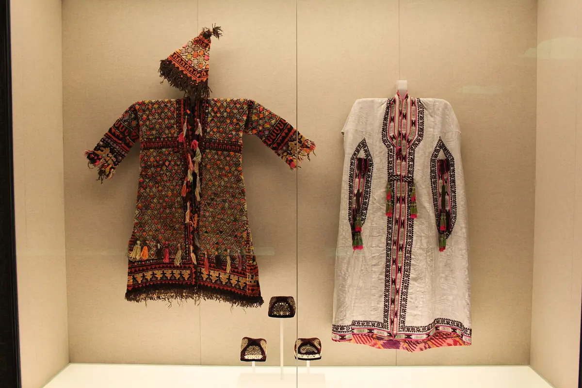 Two embroidered traditional outfits with headdresses displayed behind glass