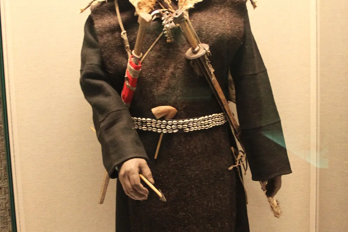 Tenue traditionnelle sombre avec épée cérémonielle et ceinture à motifs dans une vitrine de musée