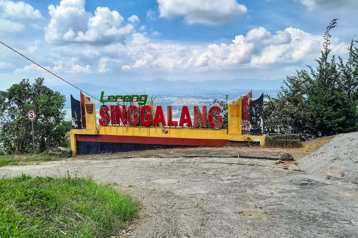 Colorful Singgalang sign beside a grassy roadside under scattered clouds