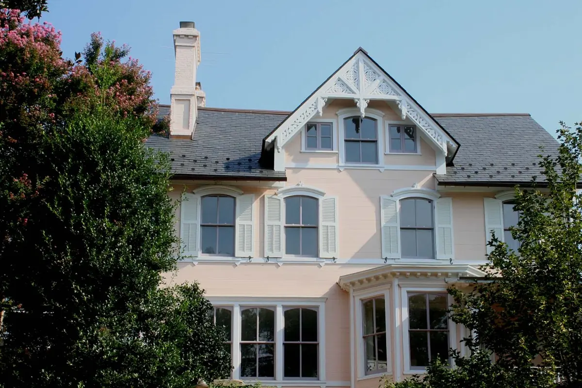 Helles Haus im viktorianischen Stil mit Veranda zwischen grünen Bäumen