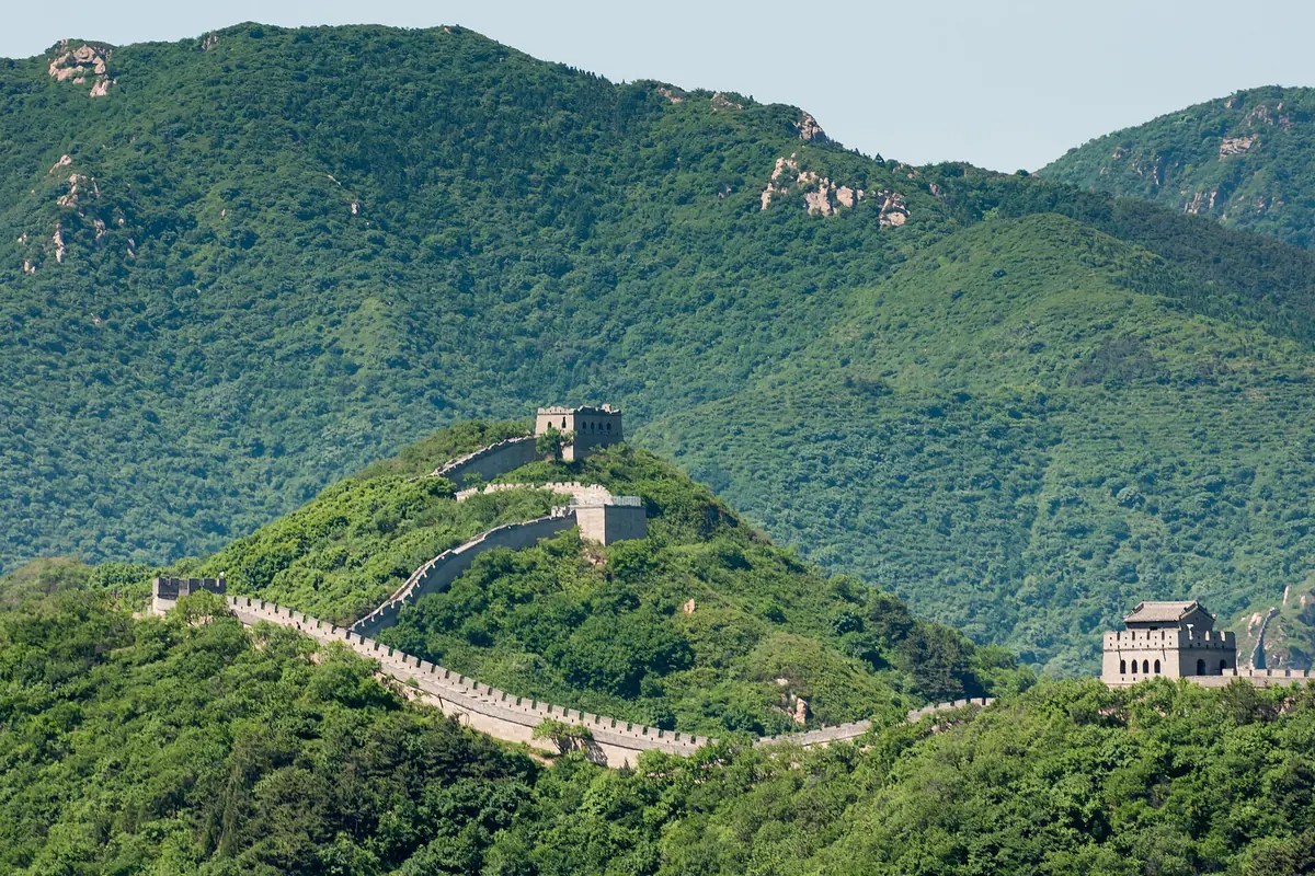 Great Wall watchtowers stepping across densely forested green mountain ridges