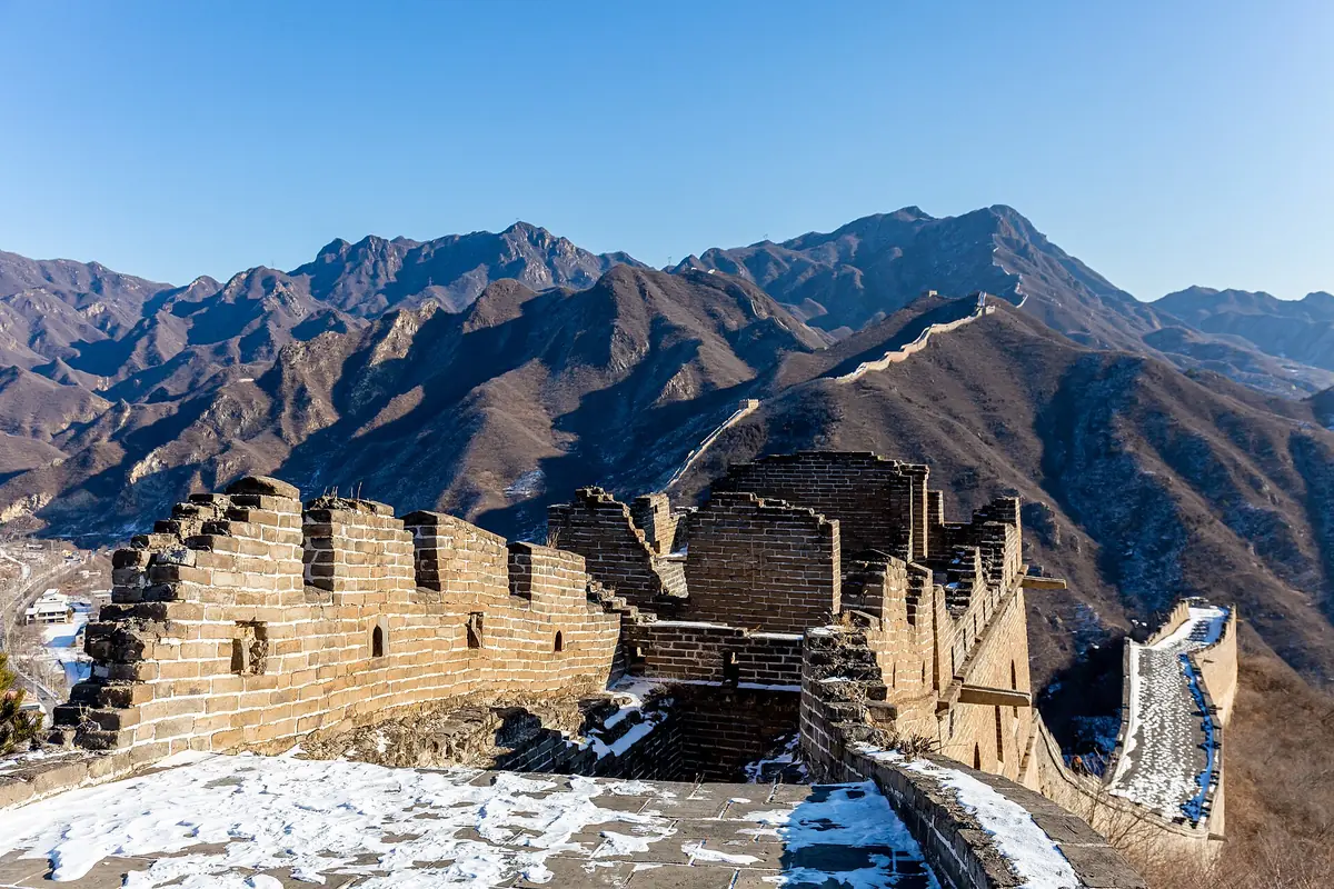 Snow on crumbling Great Wall battlements beneath rugged brown mountains