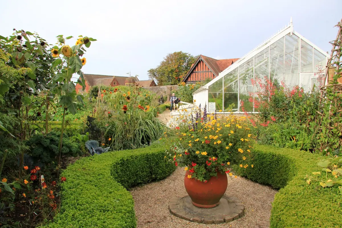 Flower garden and potted plants beside a glass greenhouse