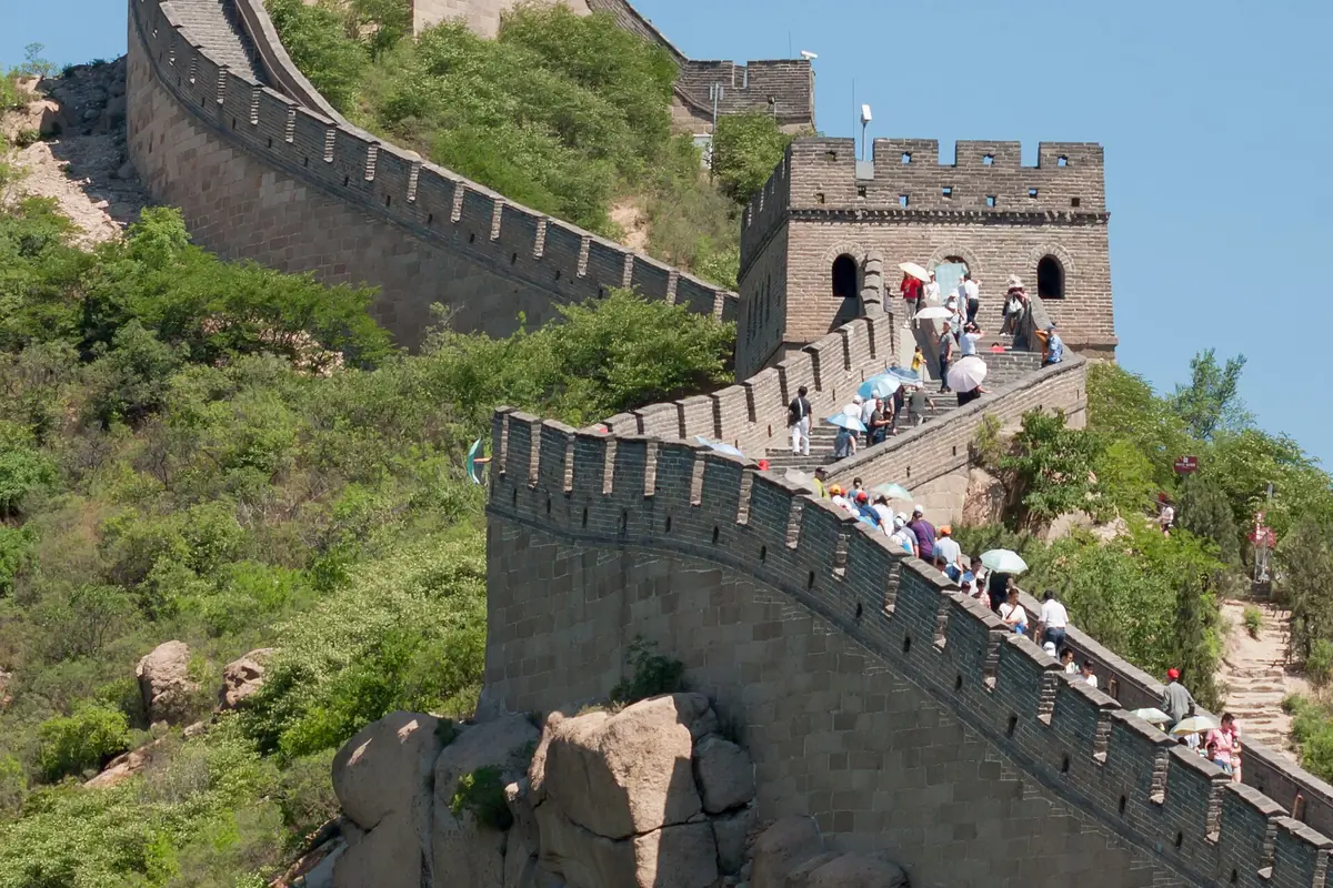 Visitors climbing Great Wall steps toward a stone watchtower on a green hillside