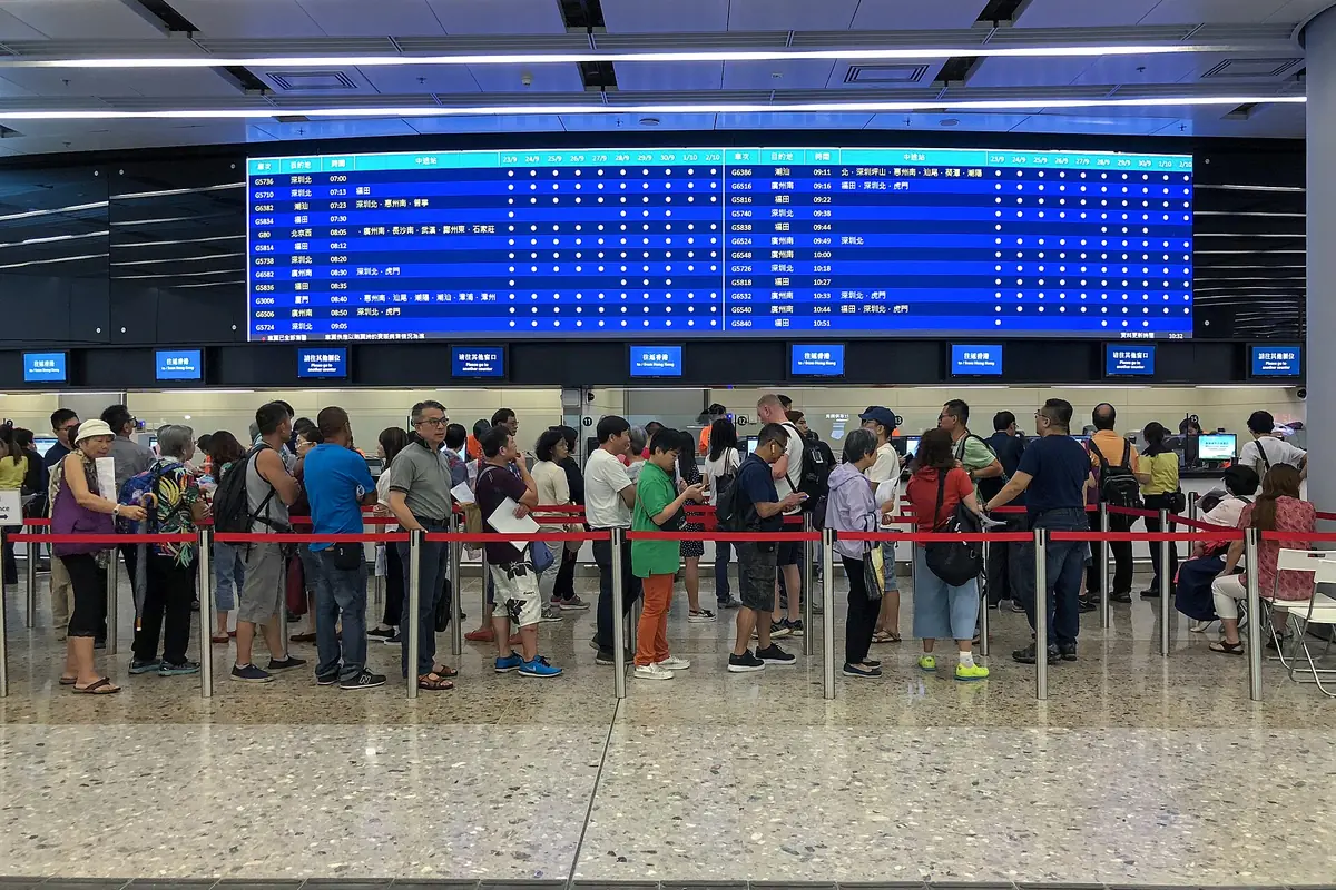 Passengers queuing beneath a blue electronic departure board in a railway station