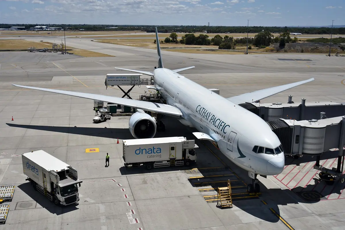 Cathay Pacific aircraft connected to a boarding bridge with ground vehicles nearby