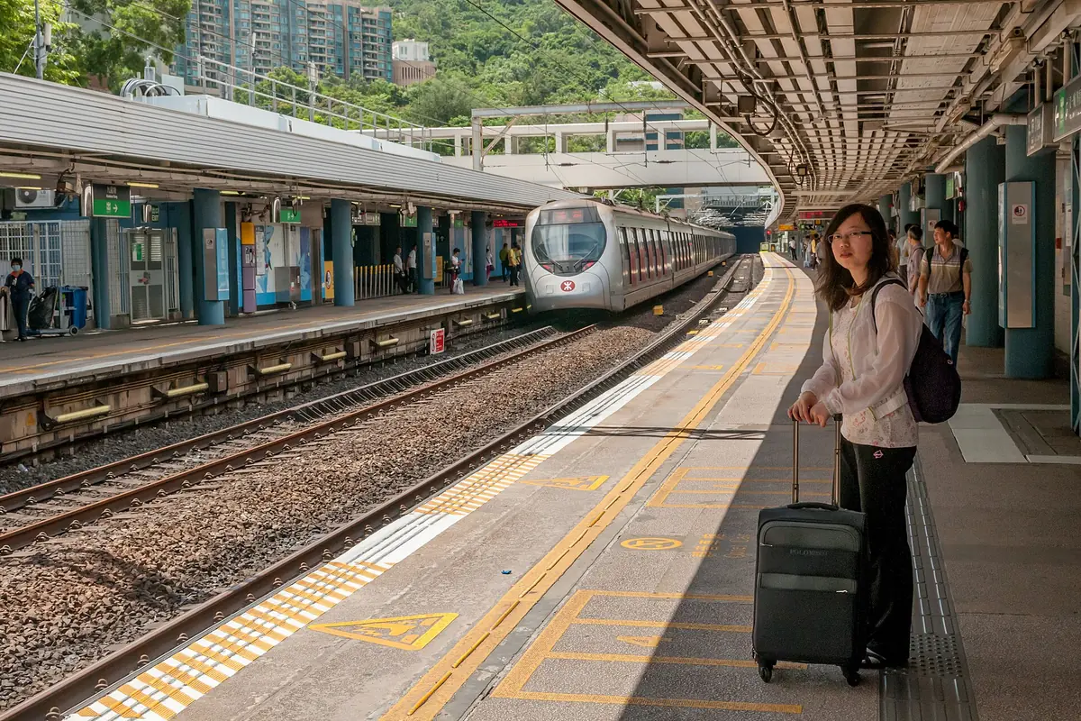 Traveler with a suitcase beside a curved railway platform and an approaching train