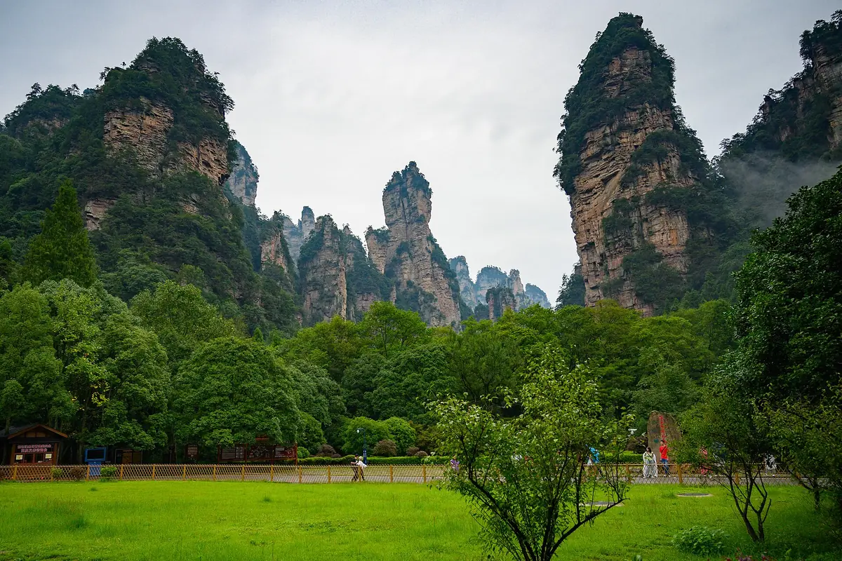 Green park and scattered pavilions beneath tall sandstone peaks in Zhangjiajie